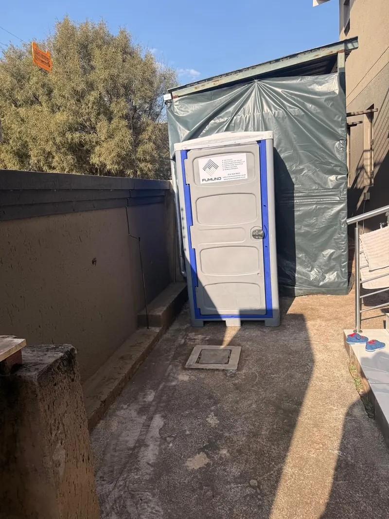Fumuno standard portable toilet unit installed in a narrow backyard passage on a residential building site in Gauteng.